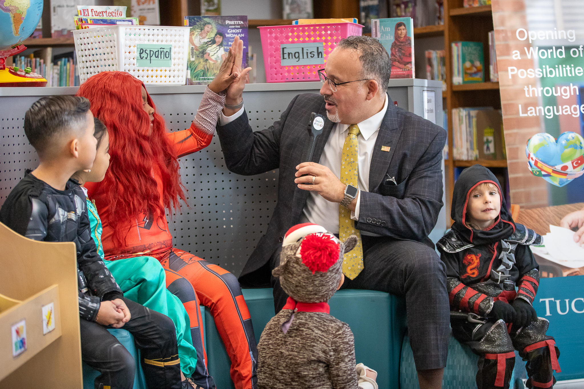 Secretary of Education Miguel Cardona high fives a student in a bright red wig