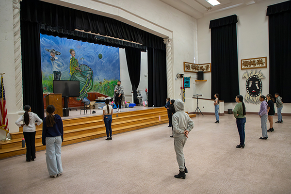 Students stand in the cafeteria looking towards the stage