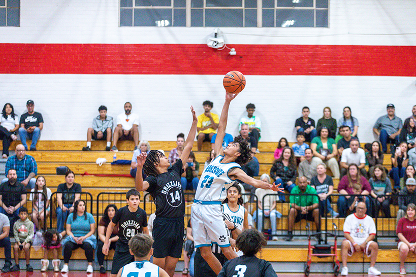 A boy holds the basketball up above his head so his opponent can't get it