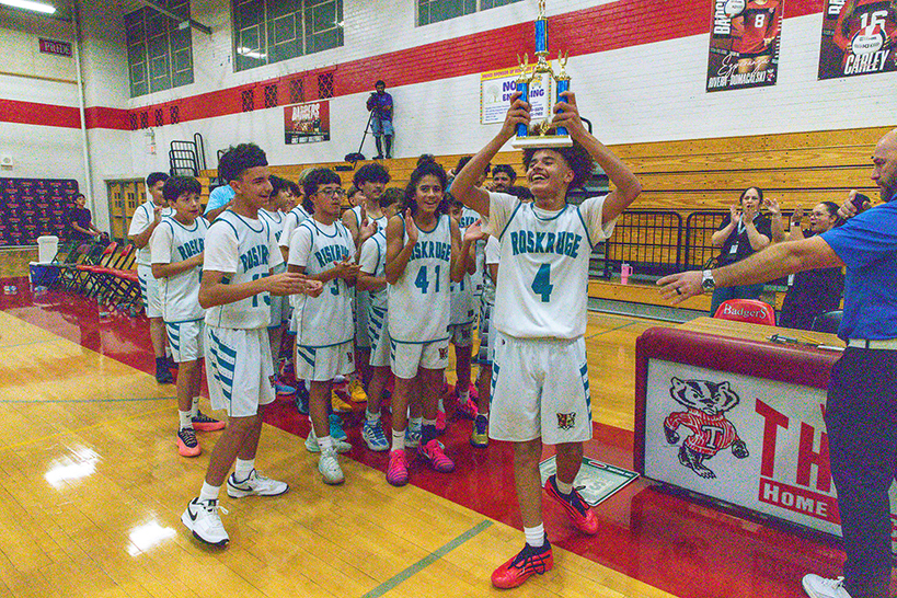 A boy holds up the trophy as his teammates cheer