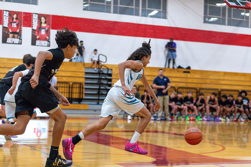 A boy chases the basketball down the court as his opponents follow behind him