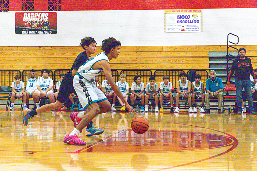A boy dribbles the ball down the court away from his opponent