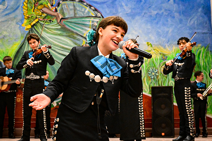 A girl sings passionately into a microphone, while the mariachi performs behind her