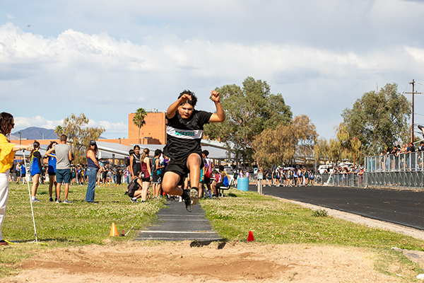 A boy jumps high in the air for the long jump