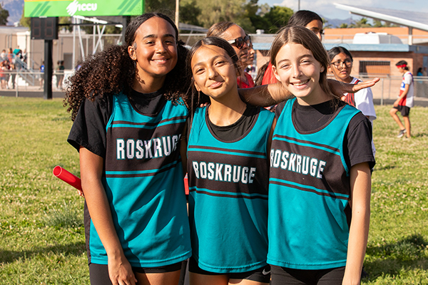 Three girls from the track team smile together on the field