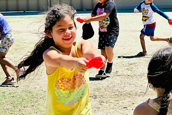 A girl smiles as she squirts her friend with a ketchup bottle filled with water
